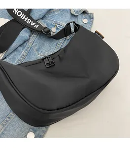 Detail of a black crescent nylon crossbody bag with dual-way zippers on denim background