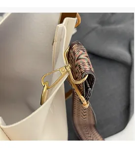Detail of high-gloss gold hardware and woven wide strap on a white leather handbag