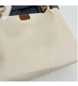 Detail of cream tote bag featuring golden chain hardware and textured woven shoulder strap