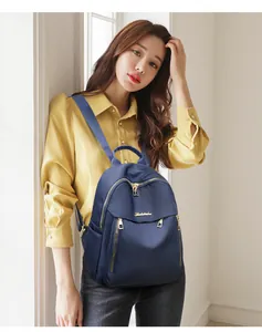 Detail of navy nylon backpack with gold hardware and multiple zipper pockets shown on model