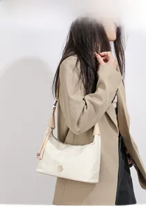Close-up of cream-colored dumpling bag with khaki strap and flower logo on model