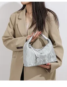 Detail of silver pleated texture hobo bag with floral charm on a khaki blazer