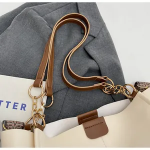 Detail of cream tote bag with brown leather handles, gold hardware, and woven strap