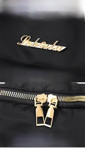 Detail of high-quality golden metal logo and smooth two-way zippers on black nylon backpack
