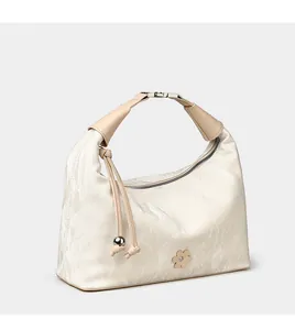 Detailed view of cream textured dumpling bag with metal flower tag and beaded charms
