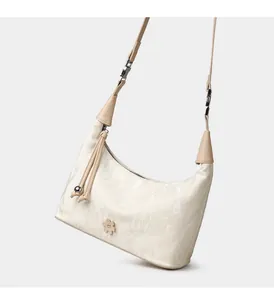 Detail of cream hobo bag showing pleated texture, flower patch, and metal tassel zip