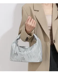 Detail of silver pleated dumpling bag with metallic flower charm and knotted strap accent