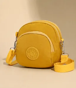 Detail van een gele nylon crossbody tas met drie ritsvakken en sportembleem voor dagelijks gebruik