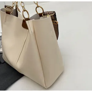 Detail of beige tote bag with gold chain handles and geometric patterned shoulder strap
