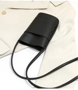 Detail of black litchi grain leather crossbody phone bag on a beige blazer background