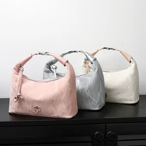 Three elegant dumpling-shaped leather handbags in pink, silver, and cream with floral charms