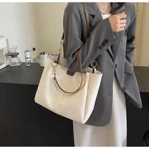 Detail of cream tote bag featuring golden chain handle and brown leather shoulder strap