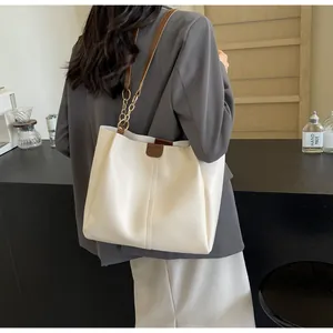 Detail view of cream tote bag with brown straps and gold chain on a cafe background