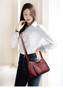 Detail of burgundy textured leather crossbody bag with multiple zip pockets on model