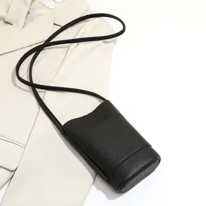 Minimalist black pebble leather mini crossbody phone bag shown with a beige blazer