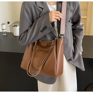 Detail of a brown leather tote bag with stylish patterned strap and metal chain handle