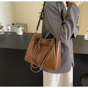 Detail of caramel leather tote bag showing woven shoulder strap and gold hardware links