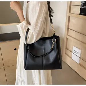 Detail of black matte leather tote bag featuring gold chain link accents and sturdy straps