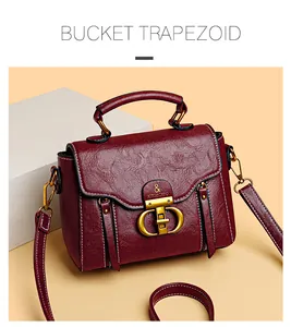 Detail of burgundy trapezoid handbag featuring textured leather and gold metal buckle