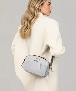 Rear view of a model wearing a light gray crossbody bag with pleated texture and brown trim