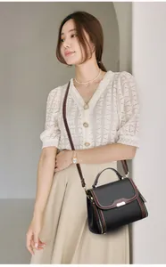 Detail of black pebbled leather crossbody bag with brown trim and gold buckle