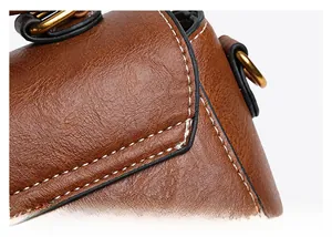 Close-up of brown lychee texture leather handbag with white double stitching and gold hardware
