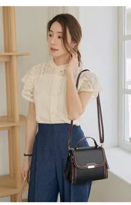 Detail of black pebbled leather handbag with brown trim and gold hardware on model