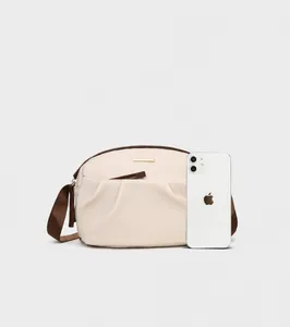 Size comparison between the beige nylon crossbody bag and an iPhone 12 for scale