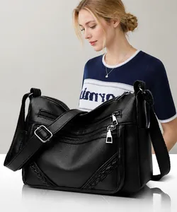 Detail van zwarte crossbodytas van generfd leer met meerdere ritszakken en geweven textuur