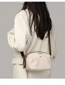 Detail view of a beige crossbody bag with adjustable brown strap on a model shoulder
