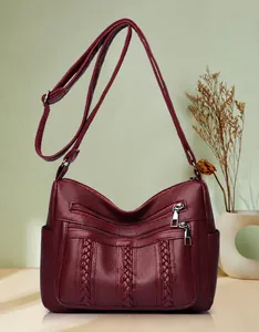 Detalle del bolso bandolera granate de cuero sintético suave con detalles trenzados y cremalleras