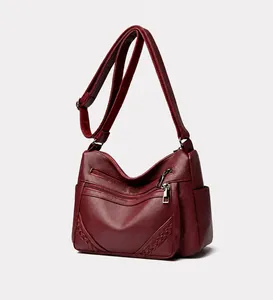 Detail van wijnrode lederen crossbody tas met geweven details en meerdere ritsen