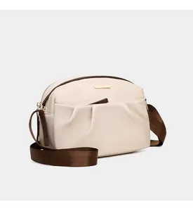 Detail view of cream oxford cloth crossbody bag with stylish pleated design and gold tag