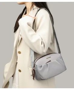Gray nylon crossbody bag with pleated detail on a white blazer model shot
