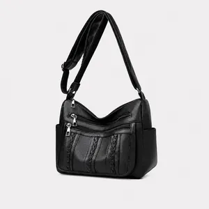 Detalle del bolso bandolera negro de cuero granulado con tres cremalleras y tejido trenzado