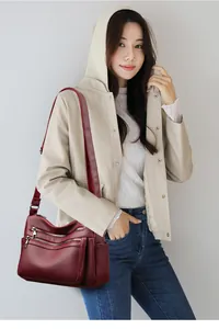 Détail d'un sac bandoulière en cuir bordeaux avec triple fermeture éclair et texture