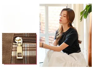 Close-up of brown plaid tote bag with polished gold zipper hardware and luxury texture