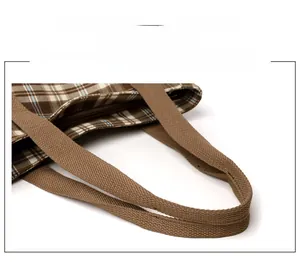 Detail of reinforced brown woven handles and zip closure on the plaid tote bag