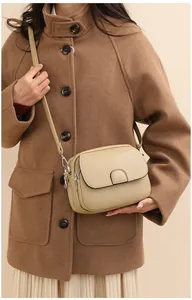 Close-up of a beige lychee-textured crossbody bag with flap on a model in a brown coat