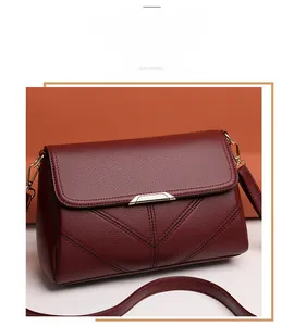 Detail of burgundy textured leather crossbody bag with V-shaped stitching and gold metal trim