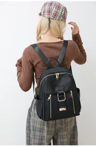 Detailed view of women's black nylon backpack with gold zippers and side pocket on model