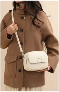 Detail view of cream lychee leather crossbody bag on brown wool coat for winter fashion