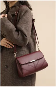 Detail view of burgundy crossbody bag with V-shaped stitching and golden metal hardware