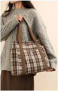 Close-up of brown plaid tote bag with side pockets and wide straps on female model