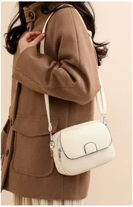 Detail view of cream crossbody bag in pebbled leather worn by a model in warm light