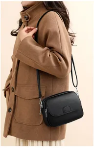 Close-up of black litchi pattern leather crossbody bag with silver hardware on camel coat