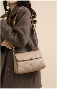Detail view of beige crossbody bag with lychee grain leather and metal clasp on coat