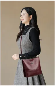 Close-up of wine red leather bucket bag with metallic kangaroo logo on a wool dress