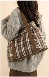 Detail of plaid tote bag with brown straps and golden snap pocket on canvas texture