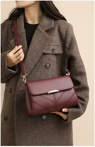 Close-up of burgundy flap crossbody bag with V-shaped stitching and metallic buckle